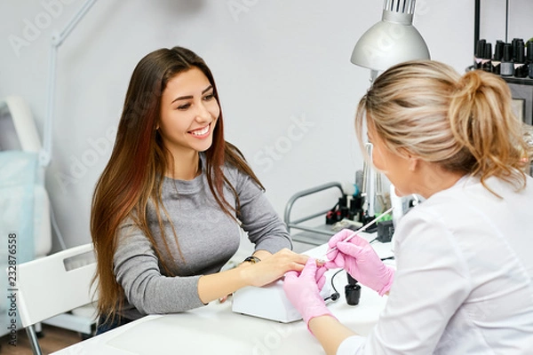 Fototapeta A nail artist does a manicure to a client. Brunette customer happy and smiling.