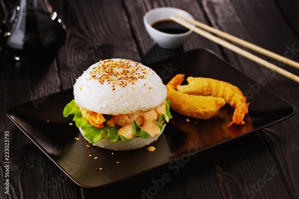 Obraz Fusion food, japanese style rice burger with tempura prawns on a black plate on black wooden background.