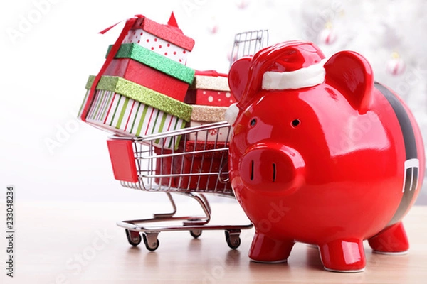 Fototapeta Christmas piggy bank next to a shopping cart full of presents