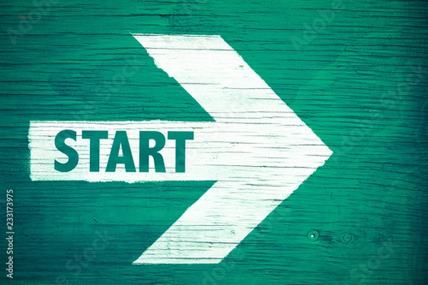 Fototapeta Start text written on white directional arrow pointing right painted on a green wooden signboard background. Motivation concept for start line for business begin and professional career path.