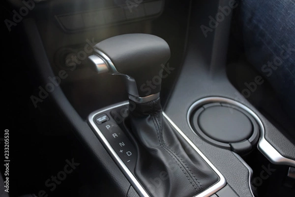 Fototapeta Car interior indoor. Black leather automatic gearbox with chrome button and sun rays, round ashtray 