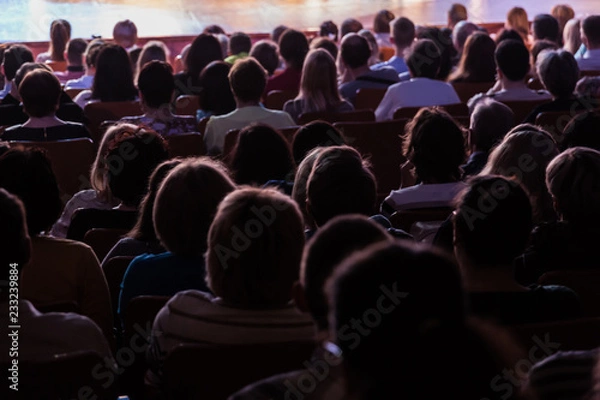 Fototapeta Spectators at a theater performance, in a cinema or at a concert. Shooting from behind. The audience in the hall. Silhouettes of people.