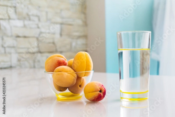 Fototapeta Clean drinking water in a glass, a bowl of apricots on the table. Healthy food.