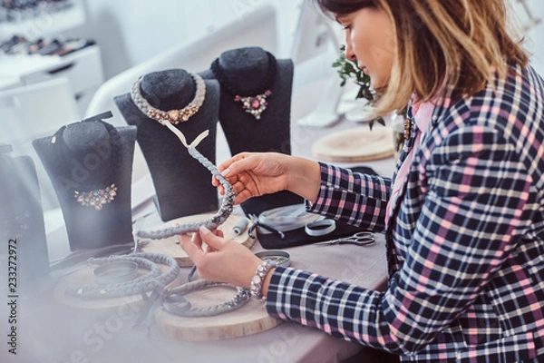 Fototapeta Elegantly dressed woman makes handmade necklaces, working with needles and thread in workshop.