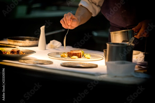 Fototapeta Chef preparing a plate made of meat and vegetables. The chef is pouring sauce on the plate.