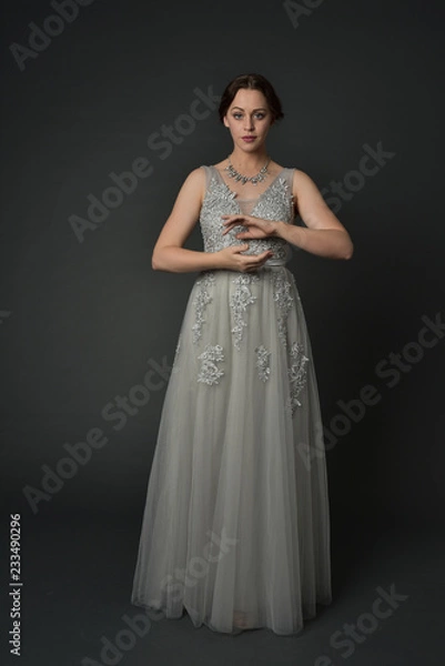 Fototapeta full length portrait of brunette  girl wearing long silver ball gown. standing pose on grey studio background.