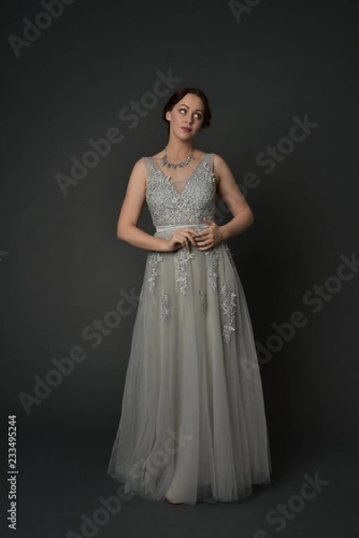 Fototapeta full length portrait of brunette  girl wearing long silver ball gown. standing pose on grey studio background.
