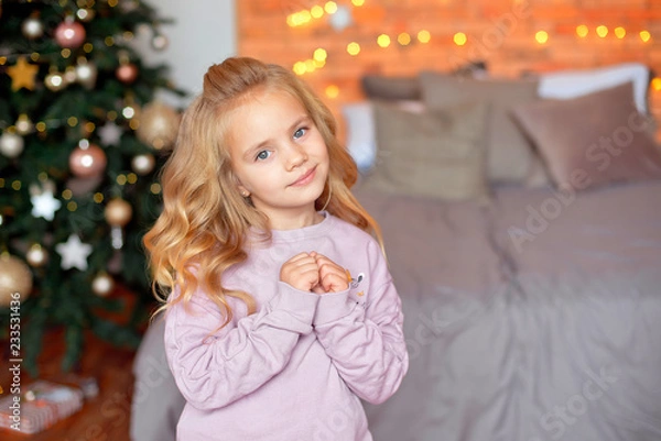 Fototapeta Beautiful girl with blond curls in anticipation of gifts in the background Christmas lights and bed . New Year and Christmas concept.