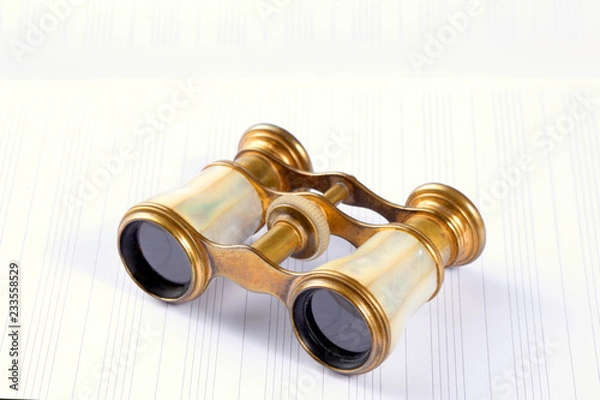 Fototapeta antique theater opera binoculars rest on an empty music score with copy space