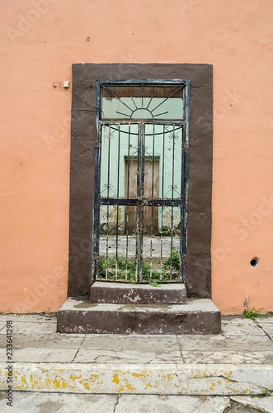 Fototapeta old wooden door with rusty bars on a wall old and broken, space for texts.