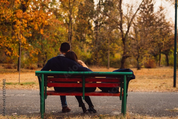 Fototapeta Boyfriend and girlfriend sitting on the bench together talking and kissing each other.