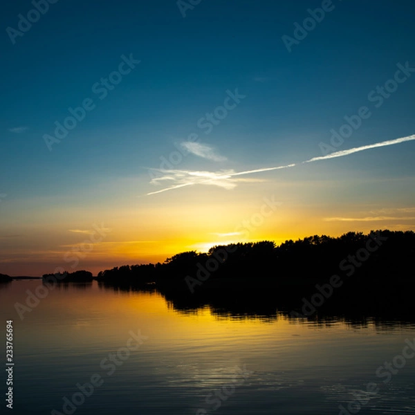 Fototapeta A beautiful deep blue sky at sunset accented by a white spangled cloud, a few days after midsummer, viewed from a cove on the Island of Nicklösa in the Åland Islands, Finland.