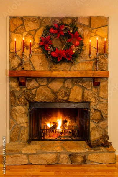 Fototapeta Stone fireplace with a glowing fire decorated with a wreath and candelabras.