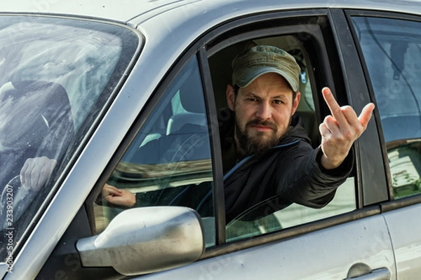 Fototapeta Sassy guy behind the wheel of a car stuck his hand out of the window and shows: " Fuck you!"