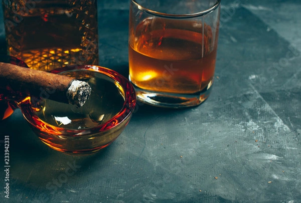 Fototapeta Strong alcoholic drink, scotch whisky in old fashion glass and decanter with smoking cigar in ashtray on gray concrete background