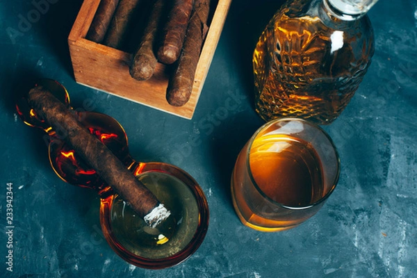 Fototapeta Strong alcoholic drink, scotch whisky in old fashion glass and decanter with smoking cigar in ashtray on gray concrete background