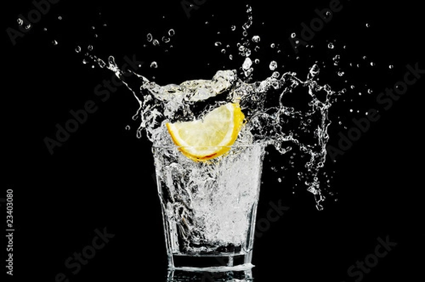 Obraz splash in a glass with lemon and ice on a black background