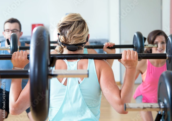 Obraz young sports group is training aerobics pump with barbell in the gym