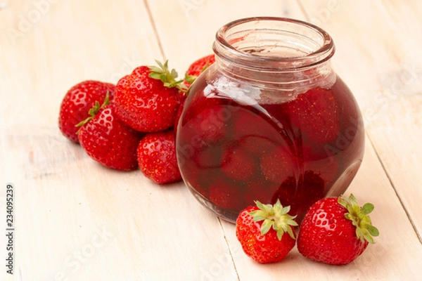 Fototapeta Strawberry jam in a jar with fresh strawberries on white wooden background. Glass jar with delicious strawberry confiture. Fresh homemade strawberry jam with berries in small jars, selective focus