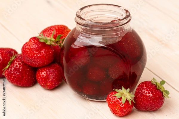 Fototapeta Strawberry jam in a jar with fresh strawberries on white wooden background. Glass jar with delicious strawberry confiture. Fresh homemade strawberry jam with berries in small jars, selective focus
