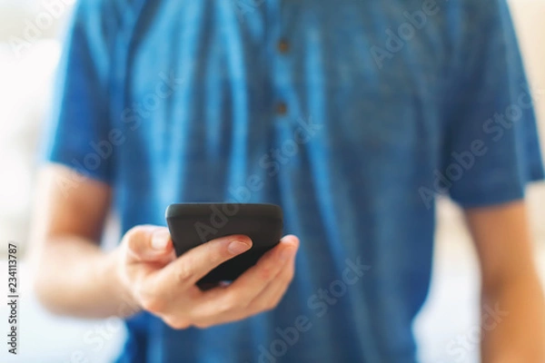 Obraz Young man using his smartphone in a bright interior room