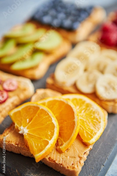 Fototapeta Six toasts with peanut butter, fresh fruits on a grey slate, stone or concrete background. Top view with copy space.