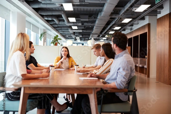 Fototapeta Group Of Young Candidates Sitting Around Table And Collaborating On Task At Business Graduate Recruitment Assessment Day