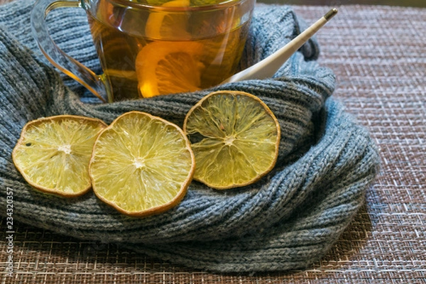 Fototapeta A Cup of tea with lemon wrapped in a soft gray scarf. Dried lemon wedges.