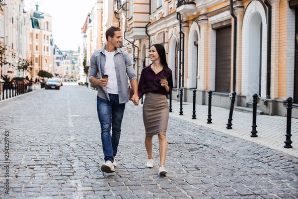 Fototapeta Multiracial couple walking in their eurotrip. Caucasian and asian ethnic, both are smiling and looking each other. They could be friends or in a relationship. Lifestyle and love concepts. Eurotour