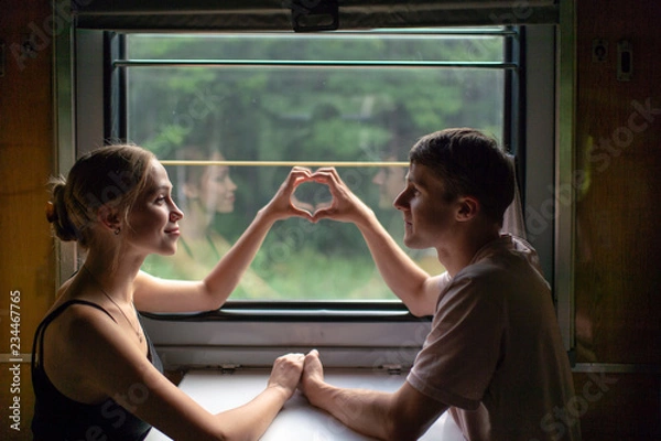 Fototapeta Couple of lovers traveling in train. Mood portrait of romantic pair in wagon looking at window with self reflections in it. Adventure on holiday of happy friends. Man and woman looking at each other.