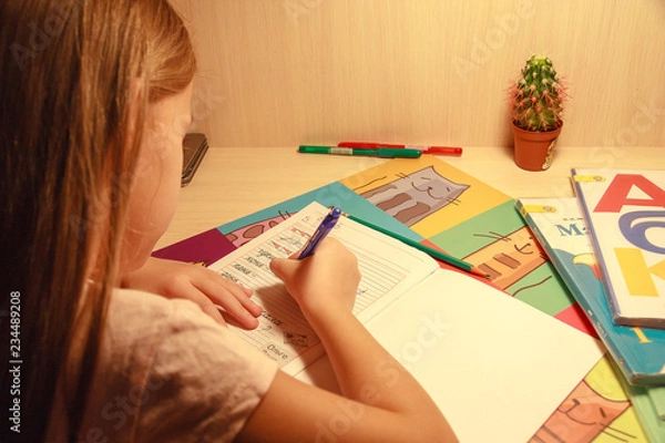 Fototapeta girl holding a pencil and writing in a notebook words and letters