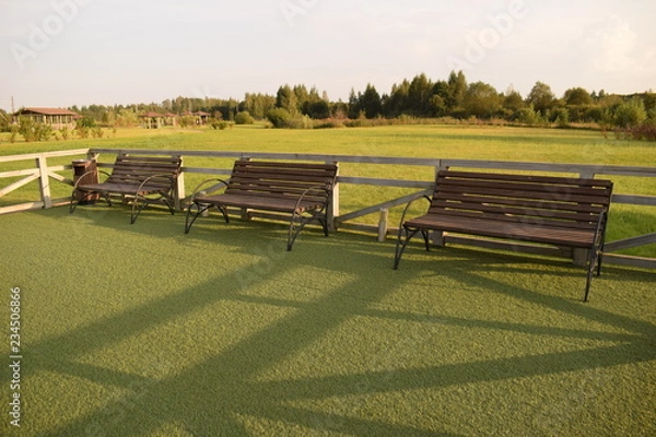 Fototapeta Wooden benches on a green field in the summer forest waiting for dreamers.