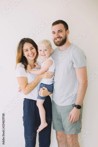 Obraz Happy young family with little son standing together in casuals near the empty wall - indoors
