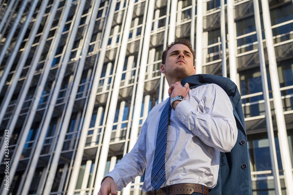 Fototapeta Businessman in classy suit holding his jacket on background of modern office skyscraper.