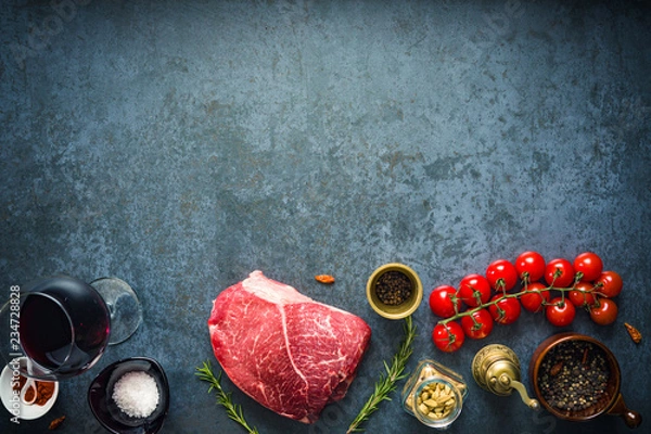 Obraz Raw marbled beef steak on dark concrete background with salt and herbs, tomatoes and glass of red wine. Top view and copyspace