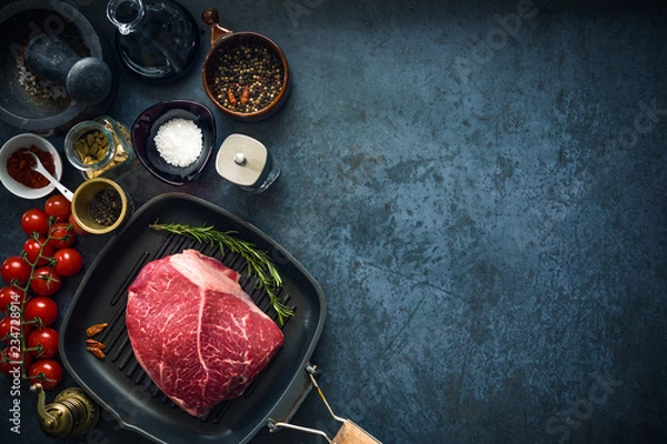 Obraz Raw marbled beef steak on a grill pan with salt, herbs and tomatoes. Top view and copyspace.