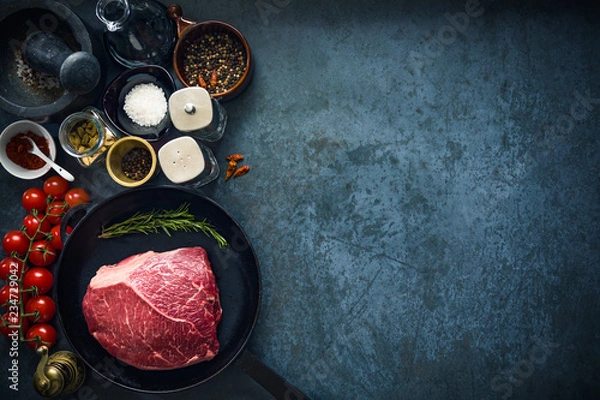Obraz Raw marbled beef steak on cast iron pan with salt and herbs and tomatoes. Top view and copyspace.
