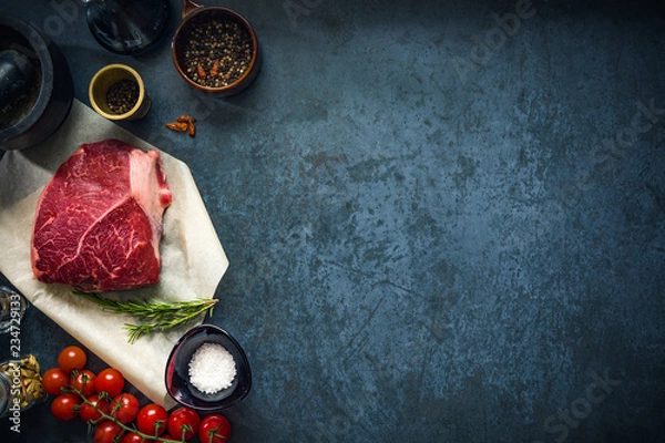 Obraz Raw marbled beef steak on dark concrete background with salt and herbs and tomatoes. Top view and copyspace.