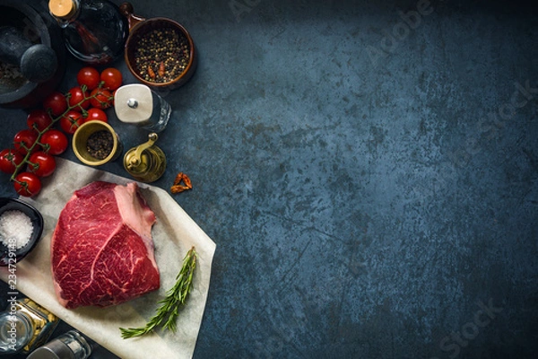Obraz Raw marbled beef steak on dark concrete background with salt and herbs and tomatoes. Top view and copyspace.