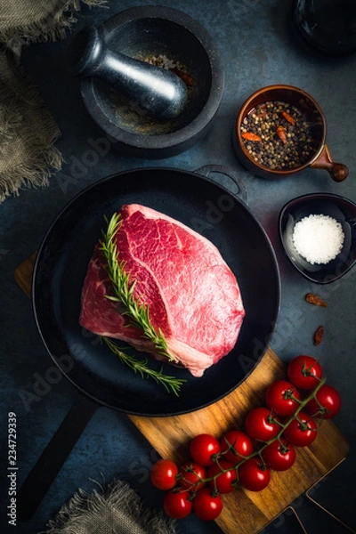 Obraz Raw Fresh Marbled Meat Beef on a cast iron pan ready for cooking on a blue concrete background top view.