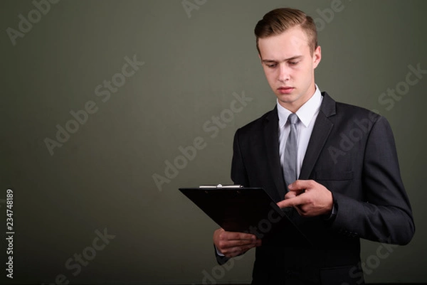 Obraz Young handsome businessman wearing suit against colored backgrou