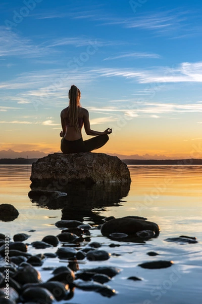 Obraz young beautiful sexy woman are doing sport fitness yoga position on a stone in the water lake sea with a wonderful sundown at the horizon - mountains and alps  and a blue sky in the background