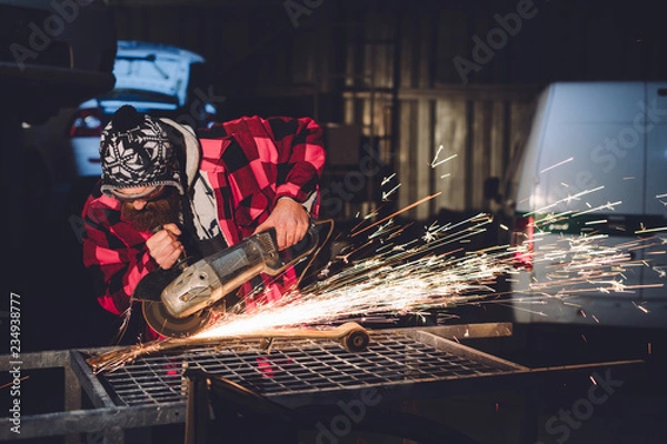 Fototapeta The employee of the service station produces body repair with a welding machine in hand sparks