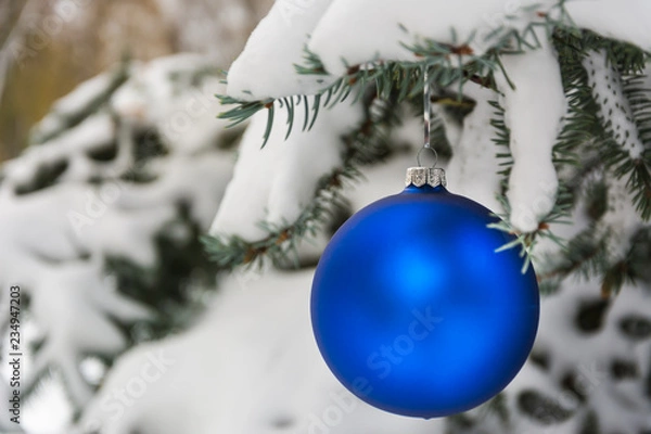 Fototapeta Blue Christmas tree ball on a snow-covered tree branch