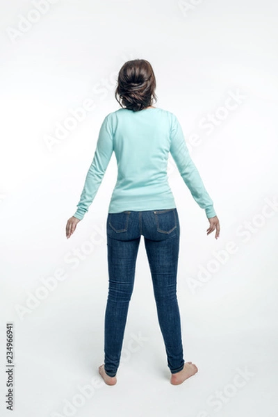 Fototapeta A young woman in a green sweater stands with her hands are down. Isolated on white background with shadow. 