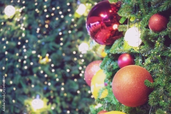 Fototapeta Closeup of red bauble hanging from a decorated christmas tree on blurred of  lights with decorated tree, sparkling and bokeh background. copy space for your text.