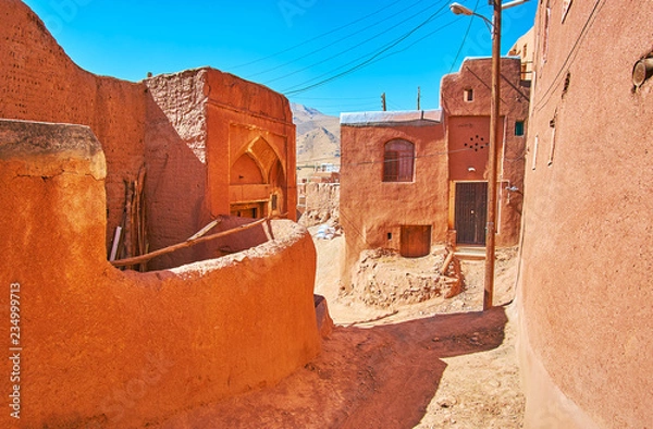 Fototapeta Zgub się wśród średniowiecznych czerwonawych budynków z błota w górskiej wiosce Abyaneh z zachowanymi fragmentami starożytnej architektury, Iran.