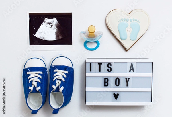 Fototapeta fla tlay pregnancy composition with space for text on white background. top view of children's accessories: snickers, pacifier, baby screen, baby projector lamp "it's a boy", delicious gingerbread