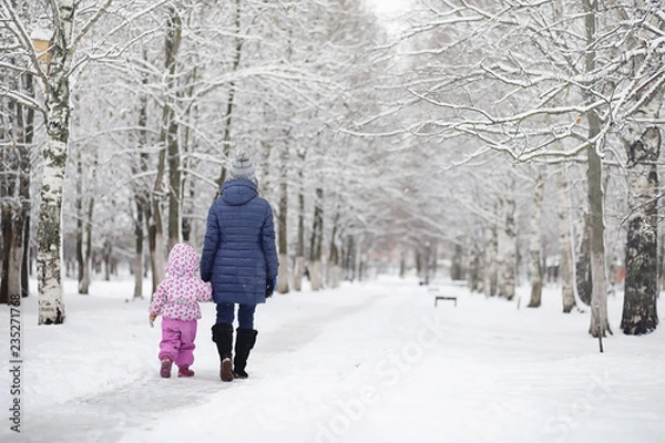 Fototapeta Snow-covered winter park and benches. Park and pier for feeding ducks and pigeons.Family on a walk in the snow covered the park.