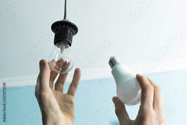 Fototapeta Incandescent lamp is changed to LED light by the hands of a man. Energy saving. 